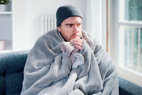 Man sitting on couch cold because of furnace problems