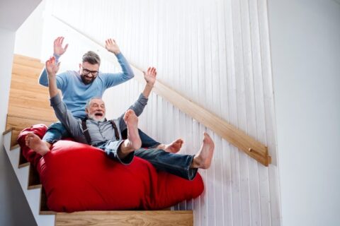 Adult father and son sliding down the stairs on a mattress