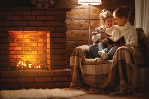 Mother and child read book on winter evening near fireplace