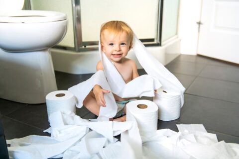 Toddler playing with toiler paper in restroom