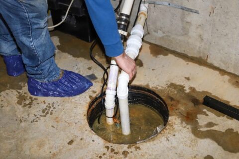 A plumber repairing a sump pump in a flooded basement.